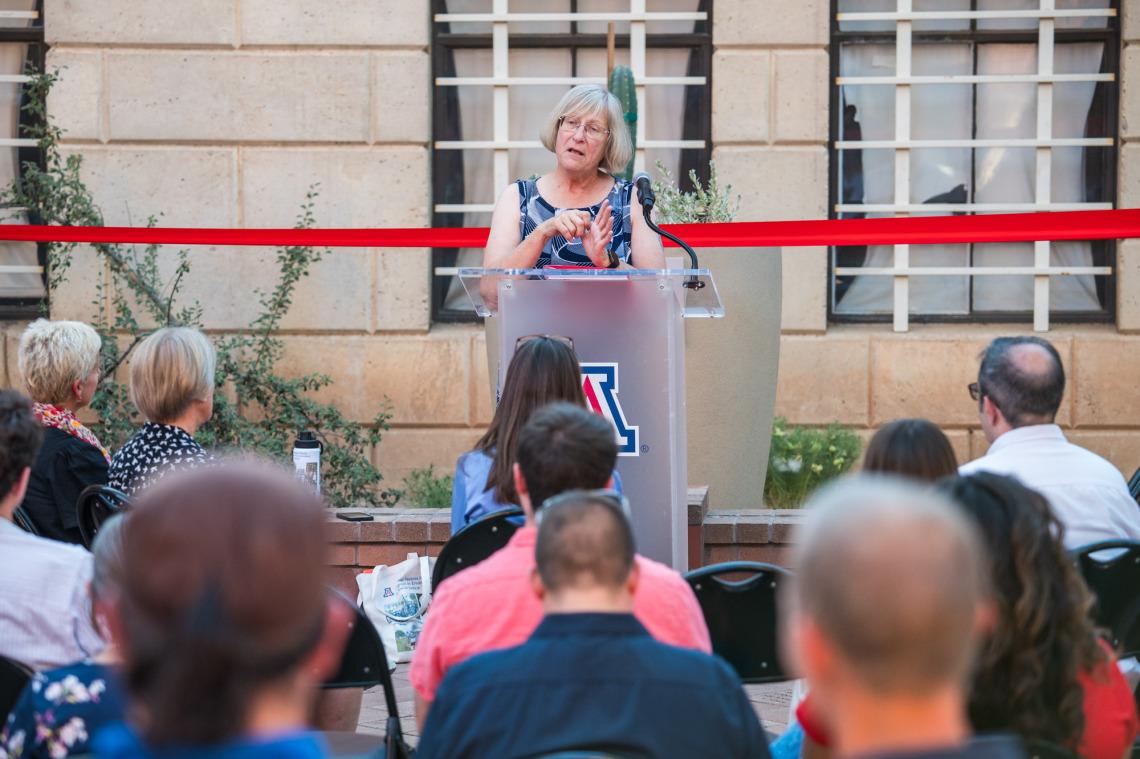 Ms. Mary Grier speaking at a podium during the event with audience members looking on.